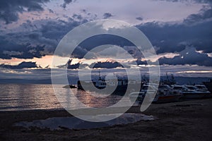 pink sunset with blue dark clouds in sky in bay of lake Baikal with jetty mole pier with old ships and boats, evening