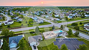 Pink sunset over suburban homes aerial green lawns neighborhood pool with parking lot