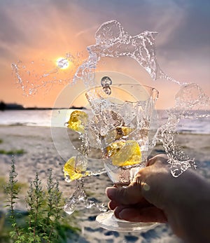 glass of water  and splas with lemon in hand on beach at pink  sunset nature landscape photo