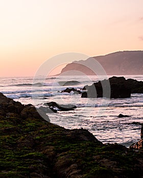 Pink sunset sky, beautiful ocean, sand  and green rocks. Portuese beach