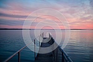 pink sunset at wooden pier on blue sea. view of long jetty stretching to the ocean. water reflection