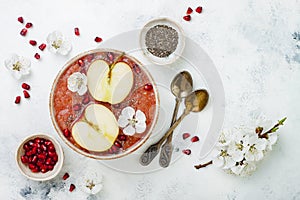 Pink superfoods smoothie bowl with chia seeds, pomegranate, sliced apples and honey. Overhead, top view, flat lay, copy space.