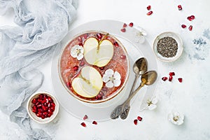 Pink superfoods smoothie bowl with chia seeds, pomegranate, sliced apples and honey. Overhead, top view, flat lay, copy space.