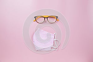 Pink surgical mask plaid and orange glasses on pink backgroud pastel style flatlay topview copyspace