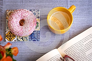 Pink and sweet glazed donut on the table, a break with a book and a cup of coffee