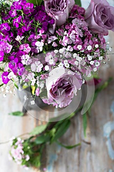 Pink sweet william flowers and lilac roses in a vase on a wooden table. Selective focus.