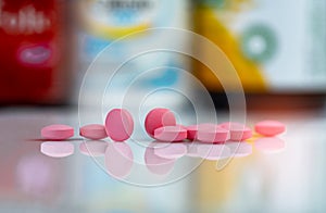 Pink tablets pills on blurred background of drug box and drug bottle. Vitamins and supplements tablets. Pharmacy drugstore.