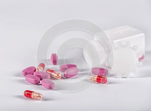 Pink tablets and red pills near the lying plastic bottle