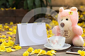 Pink Teddy Bear with coffee and book and smartphone sitting in the garden with yellow flower fall background,loneliness concept