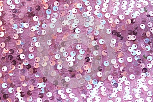 Pink textured background of shiny round multicolored iridescent sequins sewn on fabric for a trendy festive evening dress