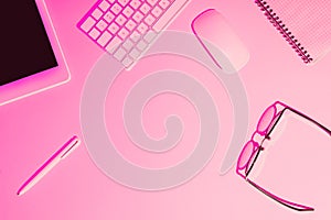 pink toned picture of pen, digital tablet, eyeglasses, textbook, computer keyboard and mouse