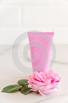 Pink tube with rose face or body cream or scrub decorated with pink core flowers. Skin care concept. Unbranding mockup