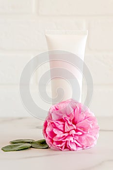 Pink tube with rose face or body cream or scrub decorated with pink core flowers. Skin care concept. Unbranding mockup