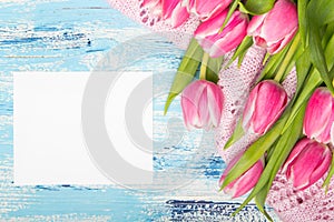 Pink tulip bouquet and balnk paper on blue wooden background,