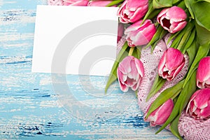 Pink tulip bouquet and balnk paper on blue wooden background, copy space.