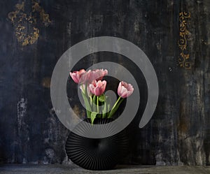 Pink tulip bouquet in black vase on table on dark background. Copy space for text