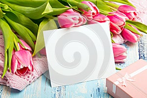 Pink tulip bouquet, gift box and balnk paper on blue wooden background,