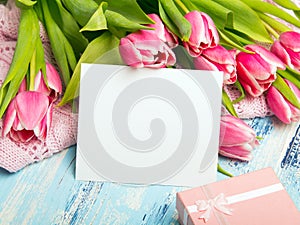 Pink tulip bouquet, gift box and balnk paper on blue wooden background