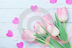 Pink tulip flowers decorated hearts and ribbon on blue table for Womans or Mothers day. Beautiful spring card. Top view.