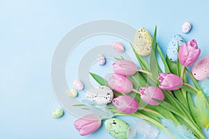 Pink tulip flowers, feathers and colorful eggs on blue table top view. Happy Easter greeting card.