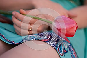 Pink tulip in the left woman hand. Girl in green dress holding a flower.