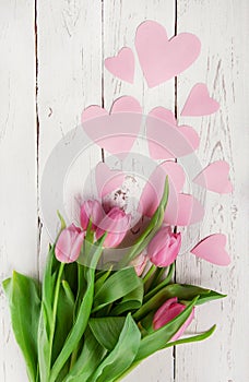 Pink tulips bouquet with paper hearts on wooden background