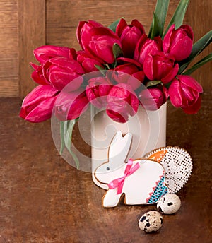 Pink tulips and easter bunny cookie on wooden background