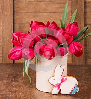 Pink tulips and easter bunny cookie on wooden background