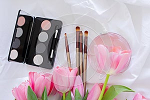 Pink tulips, eye shadow palette, brushes and perfume bottle on white background, women makeup cosmetics set