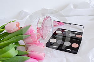 Pink tulips, eye shadow palette with mirror and perfume bottle on white background, women cosmetics set