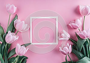 Pink tulips flowers and sheet of paper over light pink background. Saint Valentines Day frame or background.