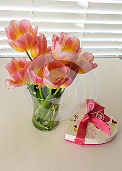 Pink tulips in full bloom in vase with Valentine candy box beside it on table