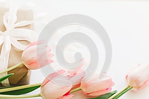 Pink tulips and gift box with ribbon on white background. Stylish tender image. Happy womens day. Greeting card with space for