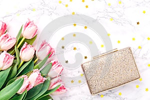 Pink tulips and golden evening clutch on white marble background. Spring and celebration concept. Copy space