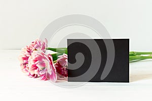 Pink tulips and horizontal black paper empty card with copy space on wooden background