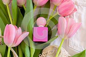 Pink tulips and perfume bottle lying on green leaves background