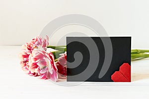 Pink tulips, red origami heart and horizontal black paper empty card with copy space