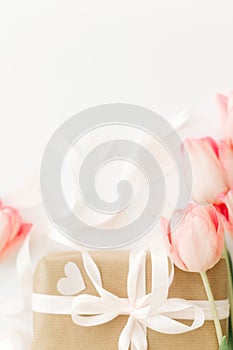 Pink tulips with ribbon and gift box on white background, flat lay. Stylish vertical image. Happy womens day. Greeting card with