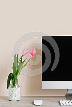 Pink tulips in a vase stand near the computer monitor. The concept of spring decor on the desktop in your home office