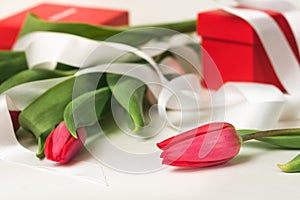 Pink tulips with white decorative ribbon on rose lettering paper and red gift boxes