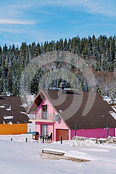 Pink two-story house with a terrace in the snow at the edge of a coniferous forest in the village