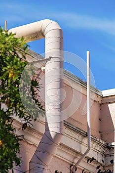 Pink ventilation pipe in partial sun and shade with foliage or trees in the yard on building with blue sky background