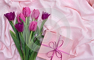 Pink, violet tulips on background with pink gift box on pink linen cloth with space for text. Holiday spring composition