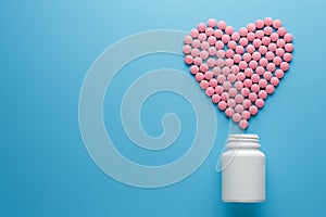 Pink vitamins B12 pills in the shape of a heart on a blue background, poured out of a white can Low contrast