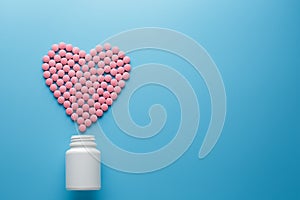 Pink vitamins B12 pills in the shape of a heart on a blue background, poured out of a white can Low contrast