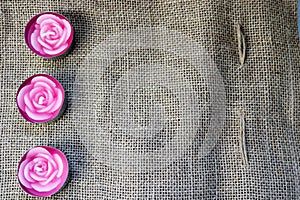 pink wax beautiful candles in the form of rose flowers with an unbaked wick on the background of an old brown canvas, harsh, unbl