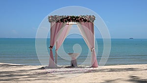 Pink wedding arch on sandy beach beside the sea