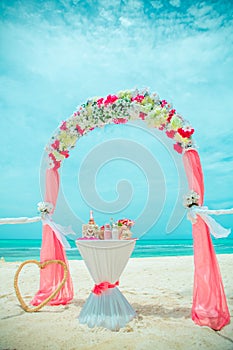 Pink wedding archway are arranged on the sand in preparation for a beach wedding ceremony.