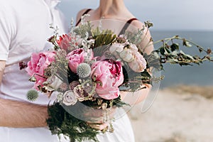 Pink wedding bouquet with a stone rose and peonies on the background of the sea.