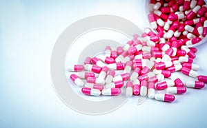 Pink and white capsules pill spilled out from white plastic bottle container. Global healthcare concept. Antibiotics drug